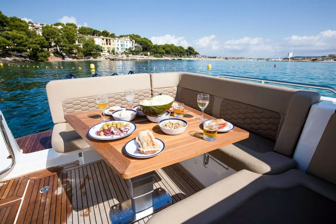 A boat table set with plates of food, including fruit and snacks, drinks, with a scenic waterfront view in the background.